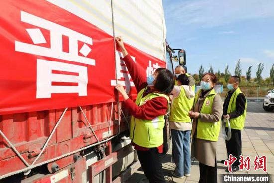 10月12日，阜康市筹集150吨价值65万元的救援物资驰援山西。图为志愿者在为物资车挂条幅。　卢浩楠 摄